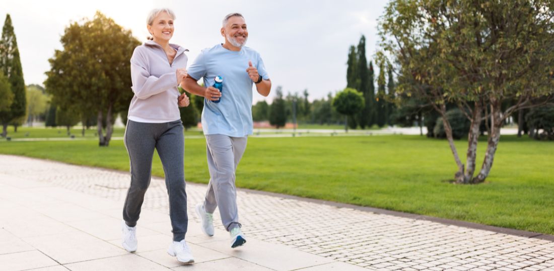 Two older adults power walking through a park