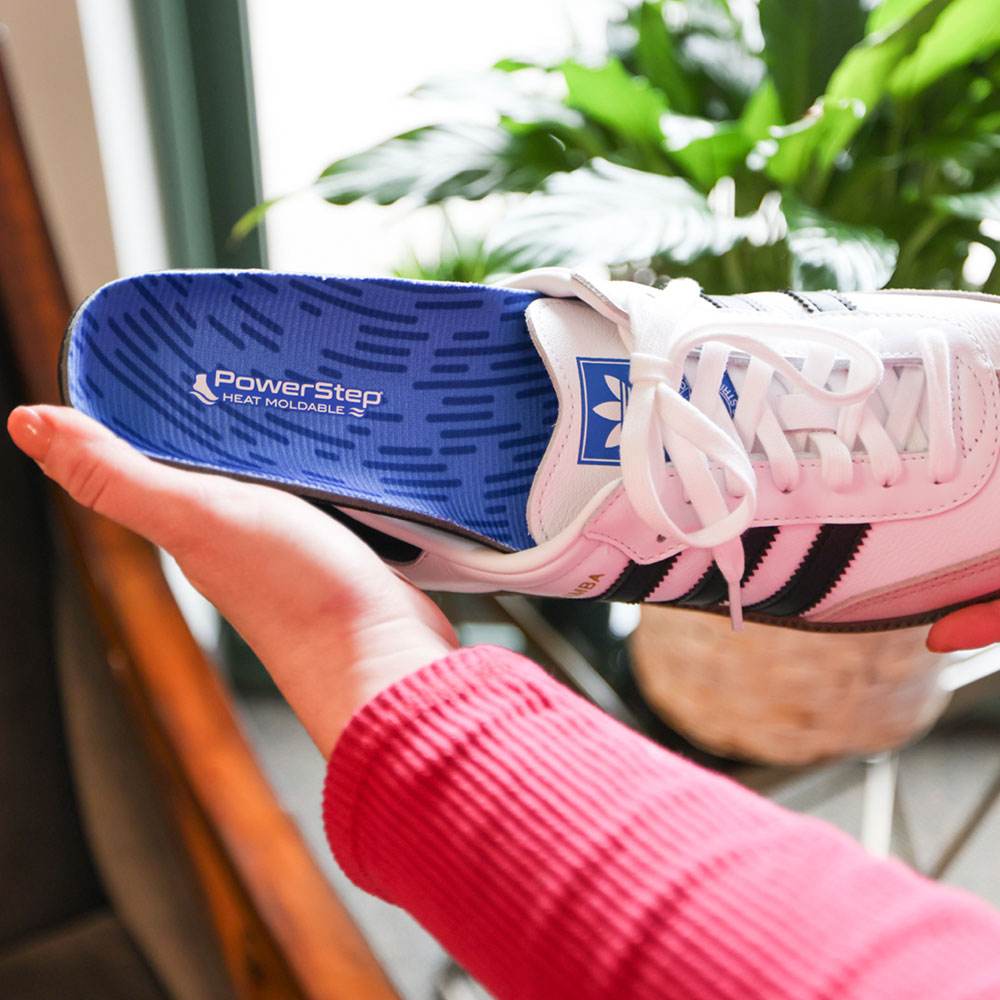 Woman placing PowerStep Heat Moldable insole into Adidas Samba shoe